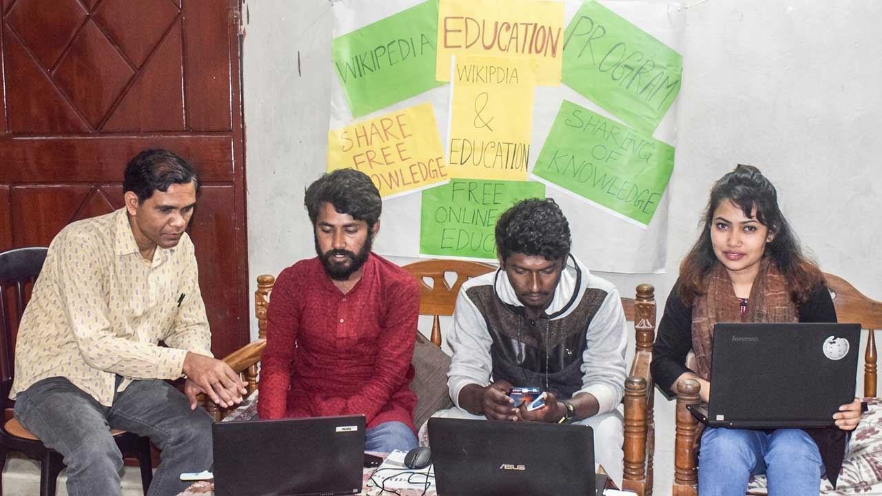 ২০২০ সালের নেত্রকোণা উইকিপিডিয়া মিটআপে উইকিপিডিয়া শিক্ষা কার্যক্রমের ব্যানার সামনে রেখে ল্যাপটপে কাজ করছেন উইকিপিডিয়ানরা।
